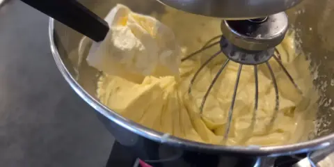 Préparation d'une crème mousseline chantilly onctueuse dans un robot pâtissier. Une spatule ajoute une touche de douceur.