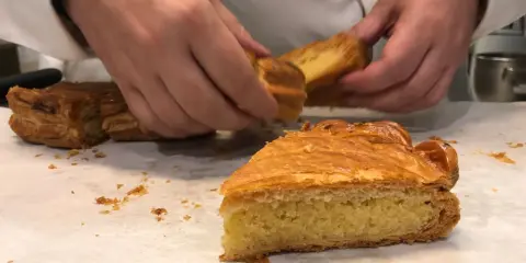 Des mains coupent une part de galette des rois, révélant sa généreuse crème frangipane dorée.
