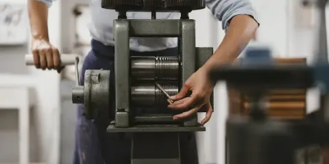 Une personne utilise un laminoir manuel pour travailler le métal. Les rouleaux sont prêts à aplatir un fil.