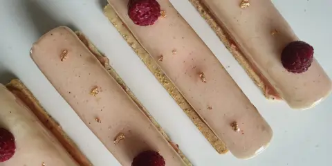 Quatre délicieux rectangles de crème chiboust ou diplomate, ornés de framboises fraîches et de feuilles d'or comestibles.
