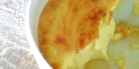 Un flan aux œufs à l'ancienne, doré et crémeux, servi dans un plat blanc sur une nappe texturée.