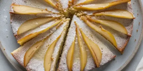 Gâteau au yaourt recette illustrée : un délicieux gâteau aux poires, saupoudré de sucre glace, prêt à être dégusté.