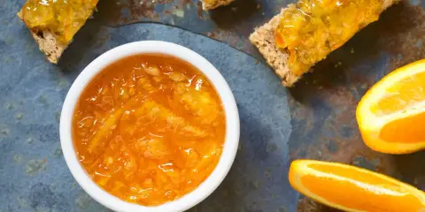 Confiture d'écorce d'orange brillante dans un bol blanc, servie sur des toasts avec des tranches d'orange fraîche.