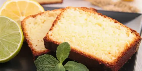 Tranches de cake au citron facile, garnies de menthe fraîche, avec des citrons et citrons verts en arrière-plan.