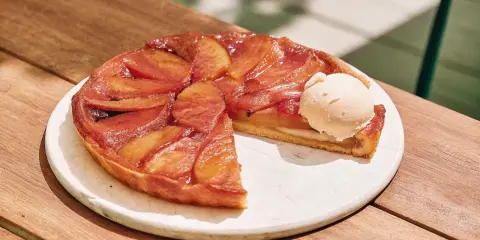 Tarte Tatin caramélisée, une part coupée, servie avec une boule de glace à la vanille. La cuisson parfaite révèle des pommes dorées et une pâte croustillante.