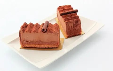 Deux parts de gâteau Trianon, le meilleur pâtissier, saupoudrées de cacao, sur une assiette blanche.
