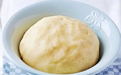 Pâte sablée prête pour la cuisson, dans un bol bleu clair. Une texture parfaite pour des tartes croustillantes.