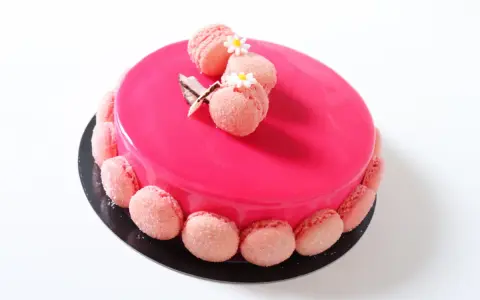Entremet fraise rose vif, décoré de macarons roses et de petites fleurs blanches.