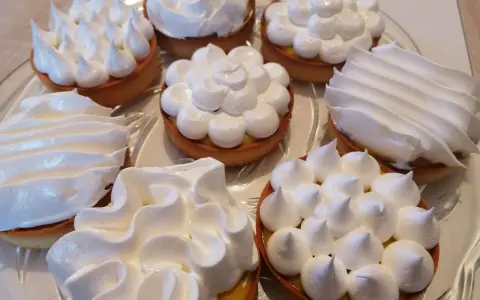 Assortiment de tartelettes garnies d'une crème citron et surmontées de **meringue italienne** aux formes variées.