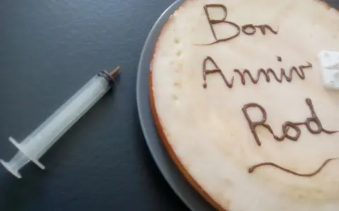 Glaçage pour écrire sur un gâteau : "Bon Anniv Rod". Une seringue est à côté, prête pour la décoration.