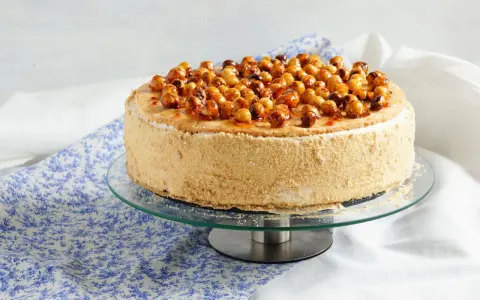 Gâteau dacquoise noisette garni de noisettes caramélisées sur un présentoir en verre.