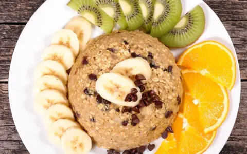 Un délicieux bowl cake flocon d'avoine garni de rondelles de banane, de tranches de kiwi et d'orange, parsemé de pépites de chocolat.