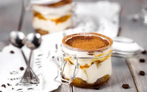 Deux bocaux de tiramisu, le meilleur dessert, saupoudrés de cacao, avec des grains de café et des cuillères sur une nappe en dentelle.