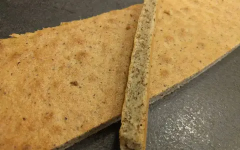 Deux fines tranches de biscuit moelleux noisette, parsemées de petits grains, reposent sur une surface sombre.