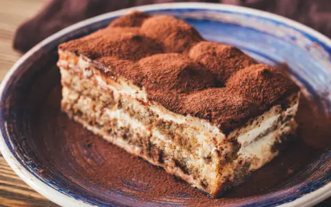 Tranche de tiramisu onctueux, saupoudrée de cacao, digne d'une recette tiramisu chef étoilé.