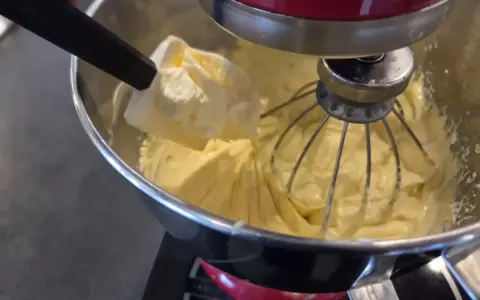 Préparation d'une crème mousseline chantilly onctueuse dans un robot pâtissier. Une spatule ajoute une touche de douceur.