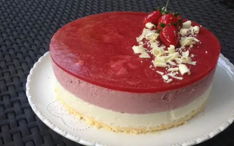 Un délicieux entremet aux trois couches, couronné d'une mousse fraise, de fraises fraîches et de copeaux de chocolat blanc. Parfait pour une occasion spéciale.