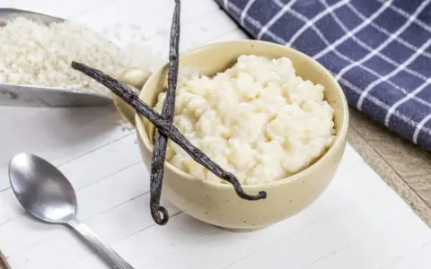 Un bol de riz au lait crémeux, garni de gousses de vanille, avec du riz brut à côté.