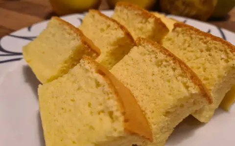 Tranches de moelleux gâteau japonais, léger et aérien, sur une assiette blanche. Des fruits jaunes sont flous en arrière-plan.