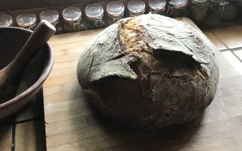 Gros pain artisanal sur une planche en bois, avec un mortier à côté. La question "peut on mélanger levain et levure" plane dans l'air.