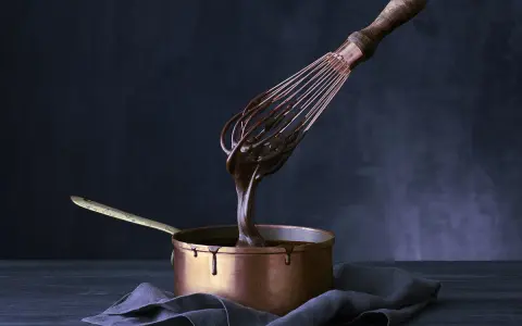 Sauce chocolat qui ne fige pas, coulante et brillante, dégouline d'un fouet dans une casserole en cuivre.