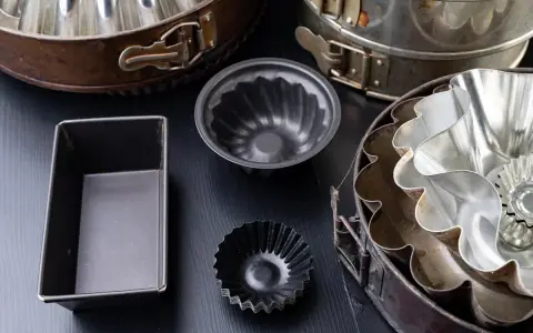 Collection de moules à gâteaux de différents types, certains en métal argenté, d'autres en métal noir, prêts pour la pâtisserie.