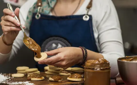 Une main dépose une cuillère de dulce de leche sur un biscuit rond, préparant des **caras crakine fait maison**.