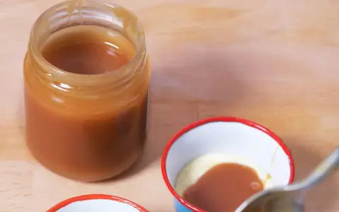 Un pot de caramel beurre salé sans beurre demi sel, prêt à être dégusté. Une cuillère est sur le point de plonger dans une petite coupelle de crème et de caramel.