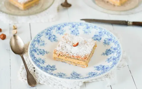 Un carré de gâteau russe, saupoudré de sucre glace et garni d'une noisette, sur une assiette ornée de bleu.