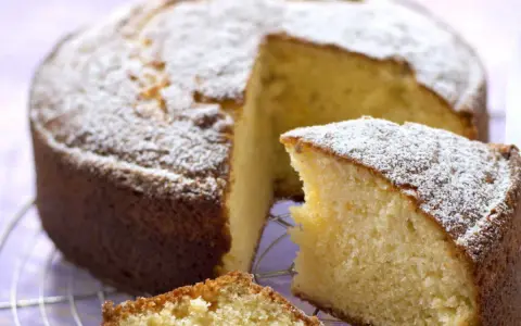 Un délicieux gâteau sans oeuf, saupoudré de sucre glace, attend sur une grille. Une part est déjà coupée, révélant sa mie moelleuse.