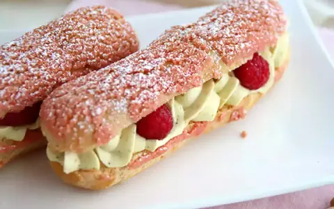 Deux éclairs à la framboise, garnis de crème légère et de fruits rouges, saupoudrés de sucre glace.