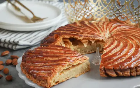 Galette des Rois dorée, garnie d'une généreuse crème d'amande. Une part est coupée, révélant sa texture feuilletée.