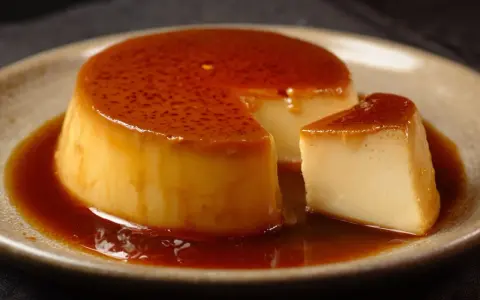Crème renversée on a plate, with a slice cut out, glistening with caramel sauce.