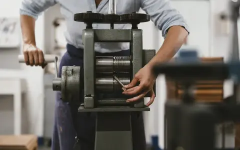 Une personne utilise un laminoir manuel pour travailler le métal. Les rouleaux sont prêts à aplatir un fil.