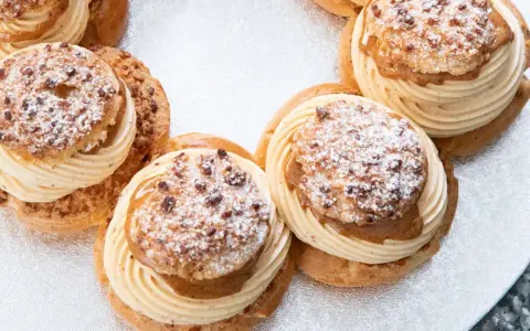 Plusieurs Paris-Brest, des pâtisseries rondes à la pâte à choux garnies de crème onctueuse et saupoudrées de sucre glace et d'amandes.