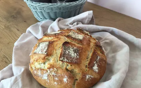 Un pain artisanal doré, prêt à être dégusté après son temps de pousse. Une corbeille de serviettes grises est visible en arrière-plan.