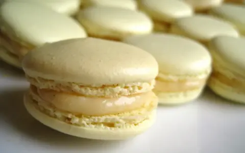Un macaron meringue italienne, délicatement garni, se tient au premier plan, entouré d'autres douceurs pâles.