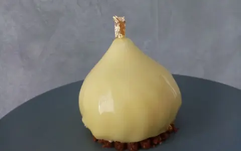 Délice en forme de poire, recouvert d'un glacage miroir jaune éclatant, sur un lit de crumble croquant, orné d'une touche de feuille d'or.
