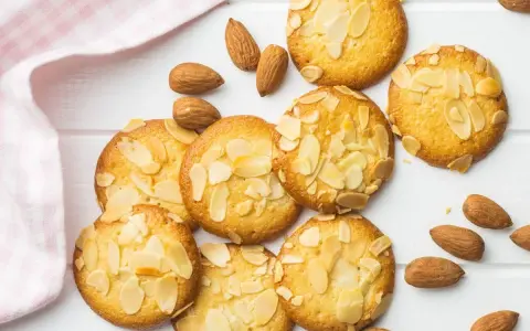 Des biscuits moelleux aux amandes, parsemés d'éclats d'amandes, sur un fond blanc avec une serviette à carreaux roses.