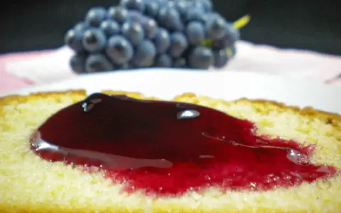 Tranche de gâteau moelleux nappée d'une généreuse gelée de raisin, avec une grappe de raisins bleus en arrière-plan.