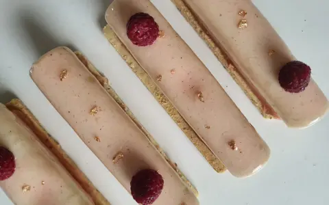 Quatre délicieux rectangles de crème chiboust ou diplomate, ornés de framboises fraîches et de feuilles d'or comestibles.