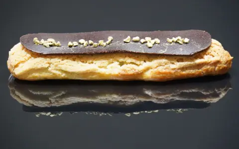 Un délicieux éclair au chocolat, garni de petits éclats dorés, repose sur une surface réfléchissante.
