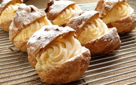 Pâte à choux au robot, garnies d'une crème onctueuse et saupoudrées de sucre glace, refroidissent sur une grille.