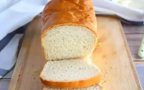 Un pain maison doré, tranché sur une planche en bois, parfait pour réussir son pain. La mie est aérée et la croûte appétissante.