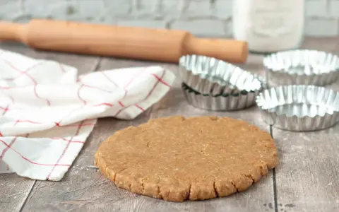 Pâte sablée prête pour la cuisson au four à chaleur tournante. Rouleau à pâtisserie, moules et torchon à proximité.