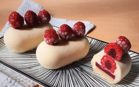 Entremets vanille-framboise sur assiette rayée, décorés de framboises fraîches.