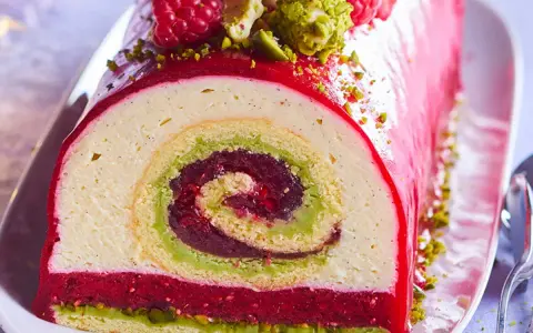 Bûche de Noël aux pistaches et framboises, un délice visuel et gustatif. La recette buche pistache framboise parfaite pour les fêtes.