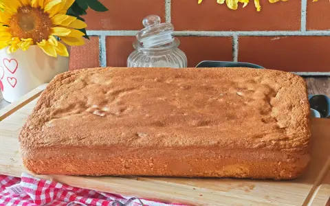 Une génoise rectangulaire dorée, parfaite pour 15 personnes, attend d'être garnie. Des fleurs jaunes et un fond de briques rouges créent une ambiance chaleureuse.