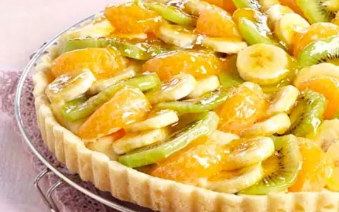 Tarte aux fruits frais sur une base de crème pâtissière. Des rondelles de banane, de kiwi et des quartiers d'orange sont disposés sur le fond de tarte.