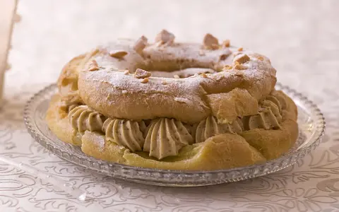 Bûche façon Paris-Brest, une couronne de pâte à choux garnie de crème onctueuse et saupoudrée de sucre glace et d'amandes effilées.